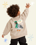 Child wearing a beige Stay Coo. sweatshirt with a pigeon in a green cap and scarf printed on the back.