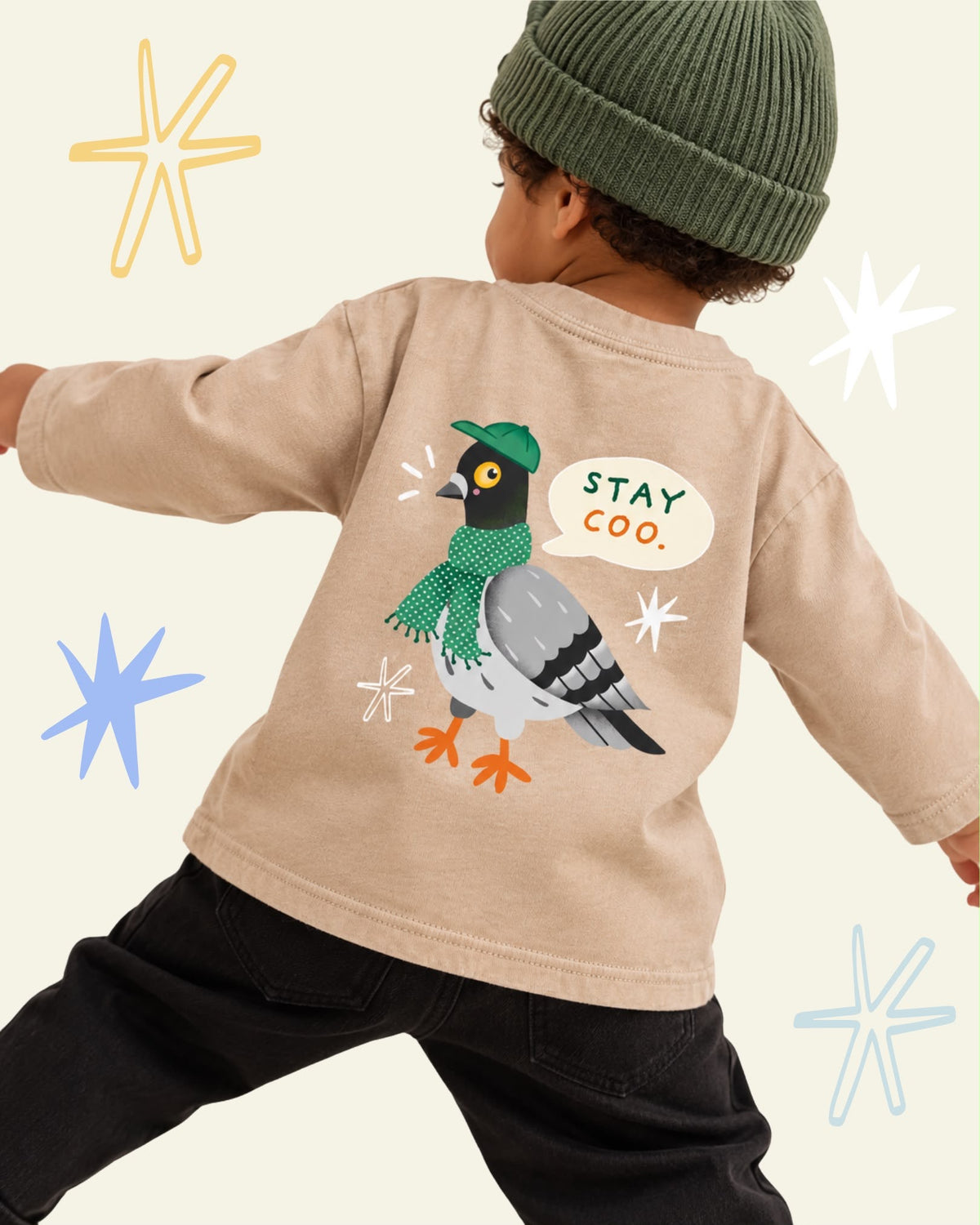 Child wearing a beige Stay Coo. long sleeve T-shirt with a large pigeon back print and a green knitted hat.