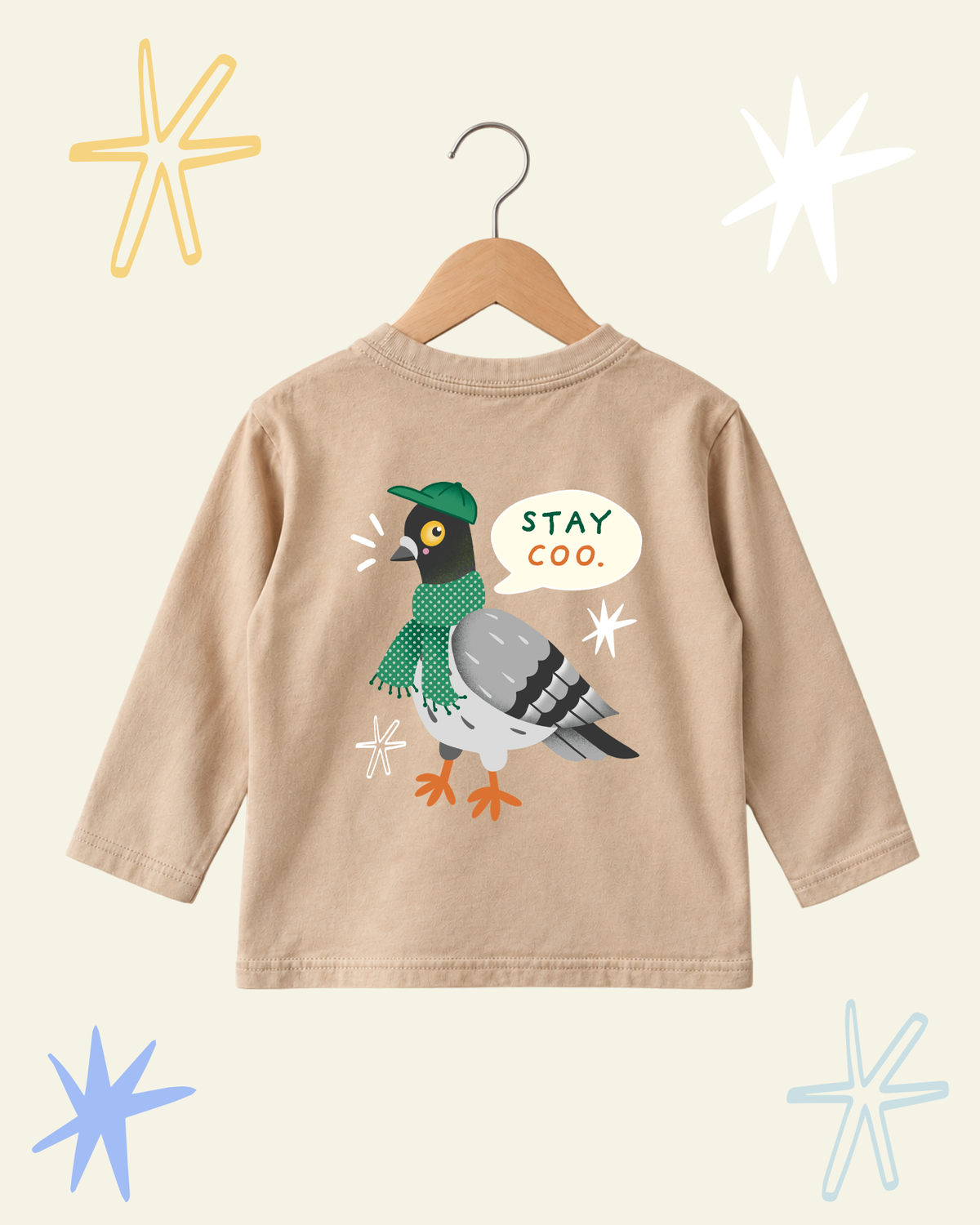 Back of beige Stay Coo. kids' long sleeve T-shirt on a hanger, with a pigeon in a green cap and scarf.