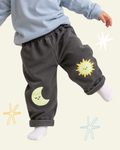Child wearing dark grey sweatpants with a smiling yellow sun and crescent moon printed on the knees.