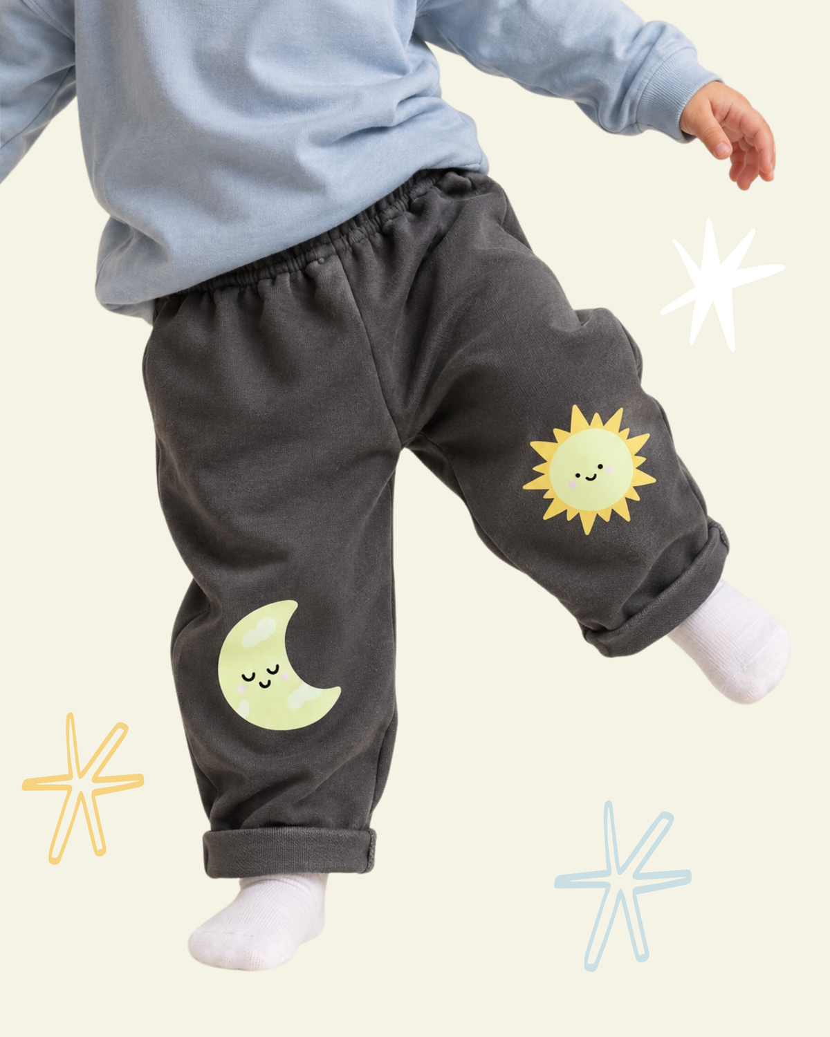 Child wearing dark grey sweatpants with a smiling yellow sun and crescent moon printed on the knees.