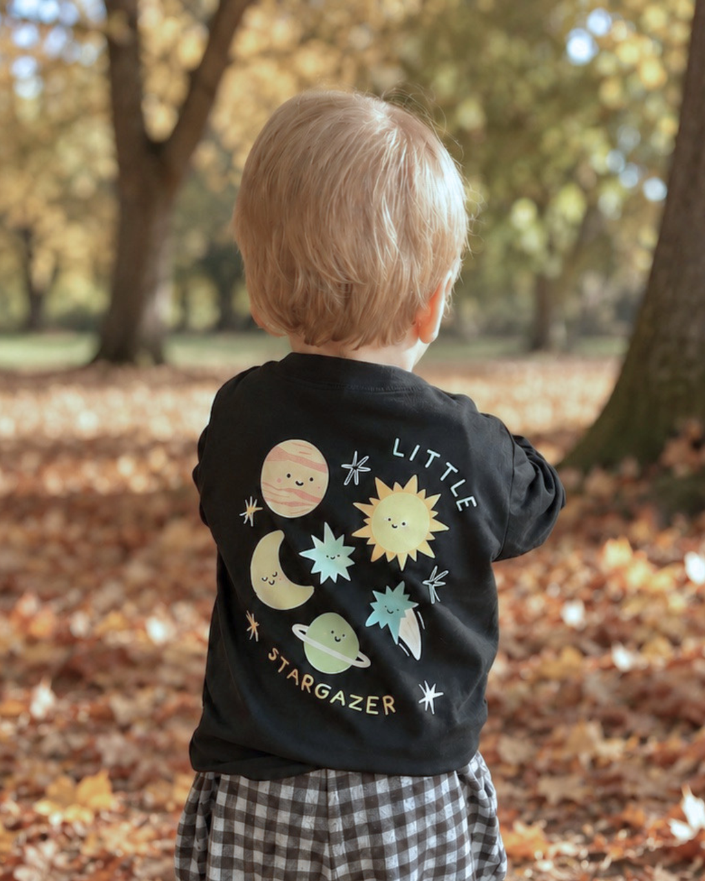 Child outdoors wearing a black Stargazer long sleeve T-shirt, showing the colourful space print on the back.